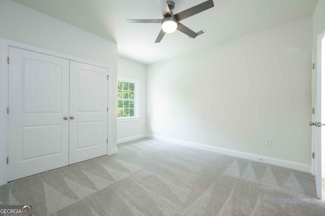 unfurnished bedroom with a closet, light colored carpet, and ceiling fan