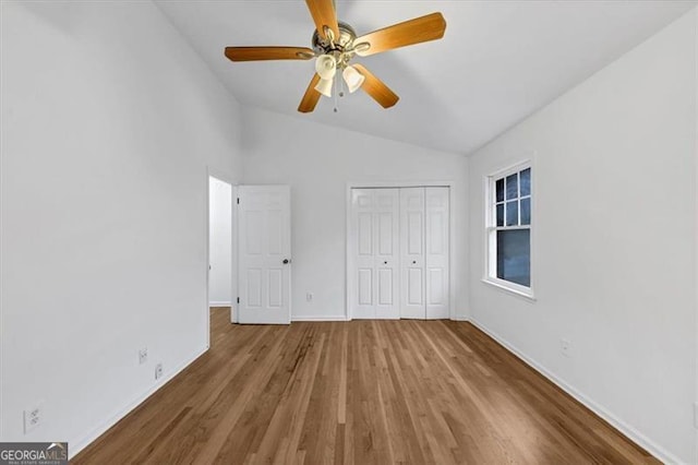 unfurnished bedroom with ceiling fan, vaulted ceiling, a closet, and hardwood / wood-style flooring