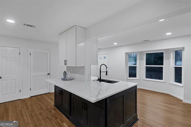 kitchen with white cabinets, light hardwood / wood-style flooring, sink, and light stone countertops