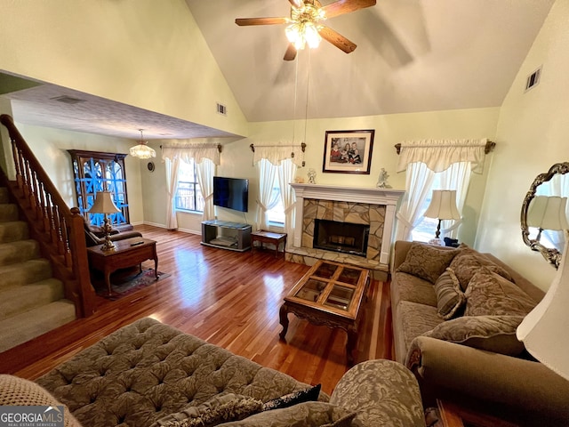 living room with hardwood / wood-style floors, ceiling fan, a stone fireplace, and high vaulted ceiling