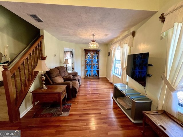 living room featuring wood-type flooring, a textured ceiling, and a notable chandelier