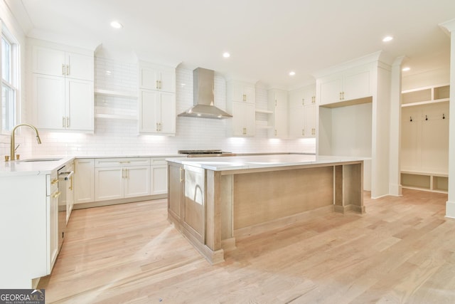 kitchen with white cabinetry, wall chimney exhaust hood, a center island, and sink