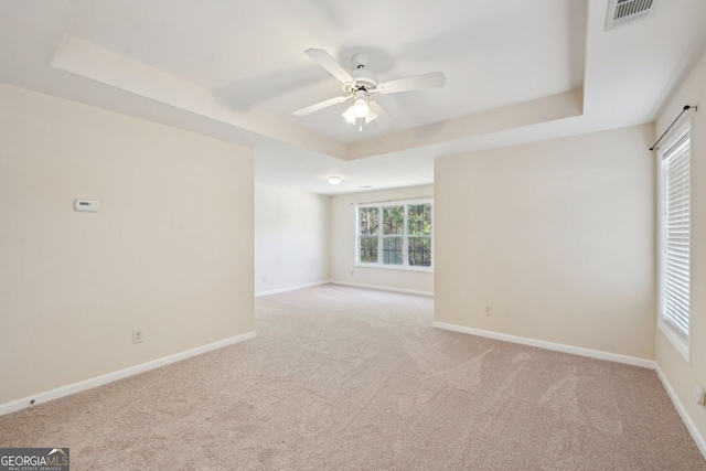 unfurnished room with ceiling fan, a raised ceiling, and light carpet