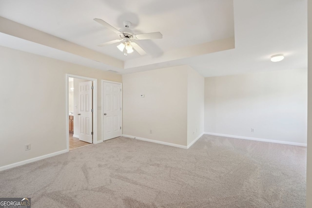 spare room with ceiling fan, a raised ceiling, and light carpet