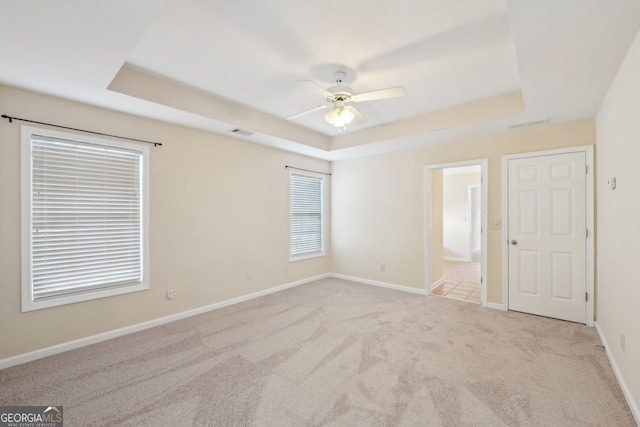 empty room with a tray ceiling, ceiling fan, and light colored carpet