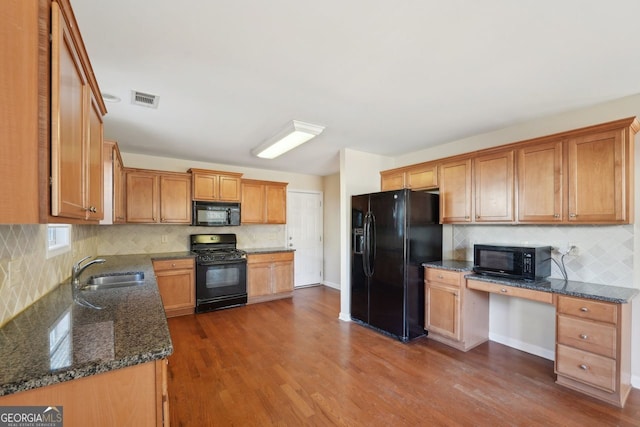 kitchen with black appliances, sink, dark hardwood / wood-style floors, dark stone countertops, and built in desk