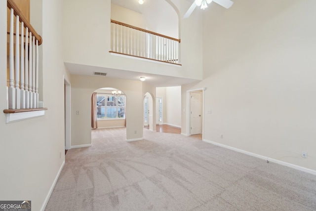 unfurnished living room with ceiling fan, a towering ceiling, and light carpet