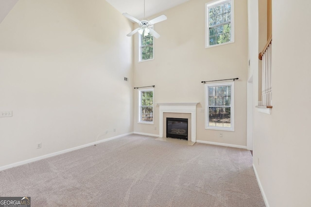 unfurnished living room featuring ceiling fan, light carpet, and a high ceiling