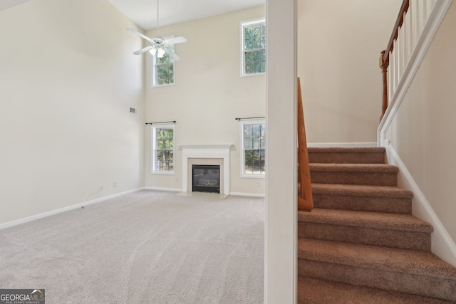 staircase featuring carpet flooring, ceiling fan, and a towering ceiling