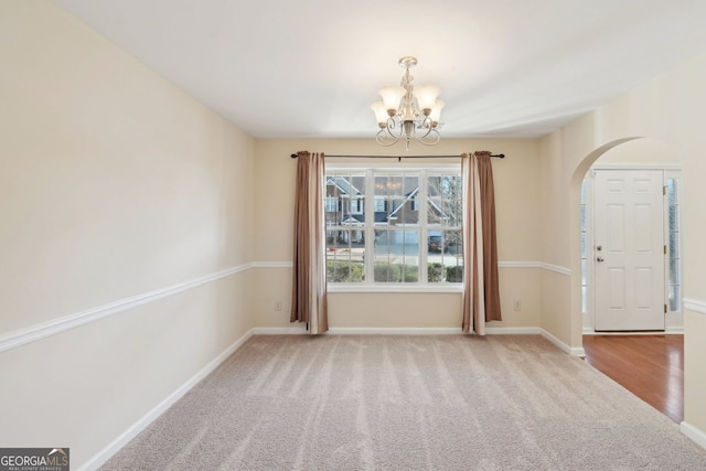 carpeted spare room featuring an inviting chandelier