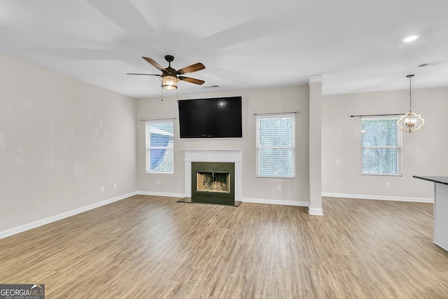 unfurnished living room with ceiling fan with notable chandelier, a wealth of natural light, and light hardwood / wood-style flooring