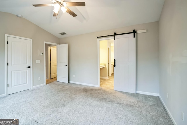 unfurnished bedroom with light carpet, a barn door, vaulted ceiling, and ceiling fan