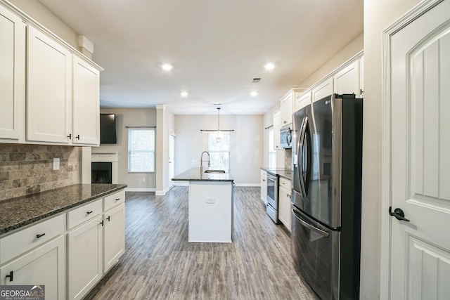 kitchen featuring appliances with stainless steel finishes, dark hardwood / wood-style flooring, dark stone counters, a center island with sink, and white cabinetry