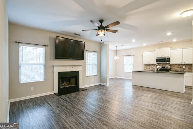 unfurnished living room featuring ceiling fan, sink, dark wood-type flooring, and a wealth of natural light