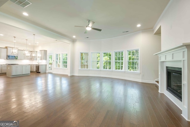 unfurnished living room featuring plenty of natural light, crown molding, and dark wood-type flooring