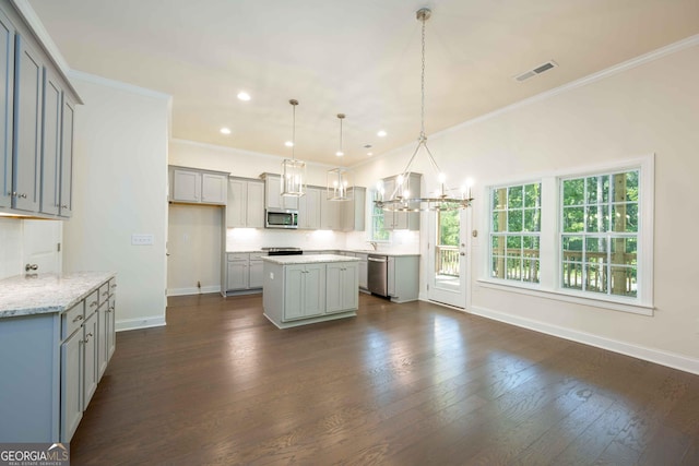 kitchen with appliances with stainless steel finishes, dark wood-type flooring, crown molding, decorative light fixtures, and a kitchen island