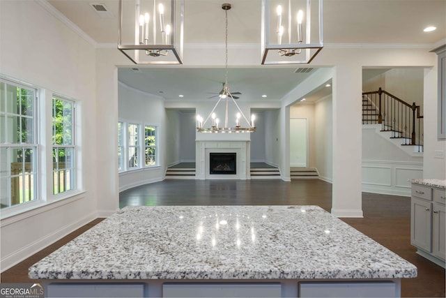 kitchen featuring a center island, crown molding, hanging light fixtures, light stone countertops, and dark hardwood / wood-style flooring