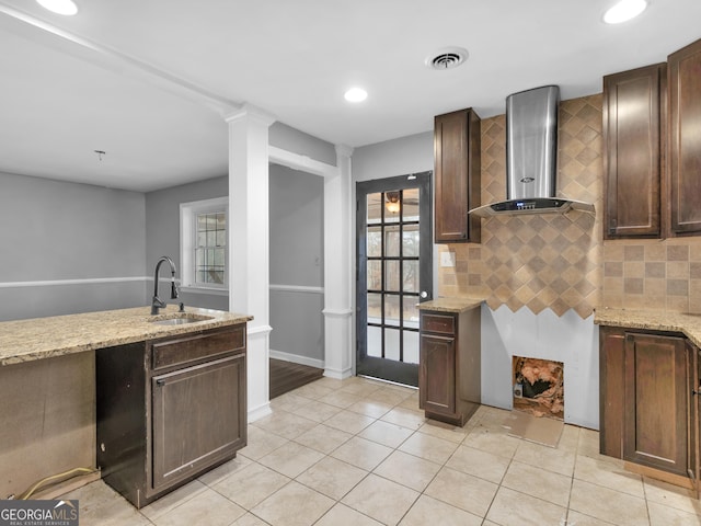 kitchen featuring dark brown cabinetry, sink, a healthy amount of sunlight, and wall chimney range hood