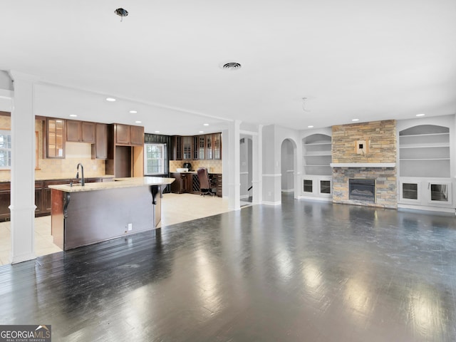 unfurnished living room with hardwood / wood-style flooring, a stone fireplace, built in features, and sink