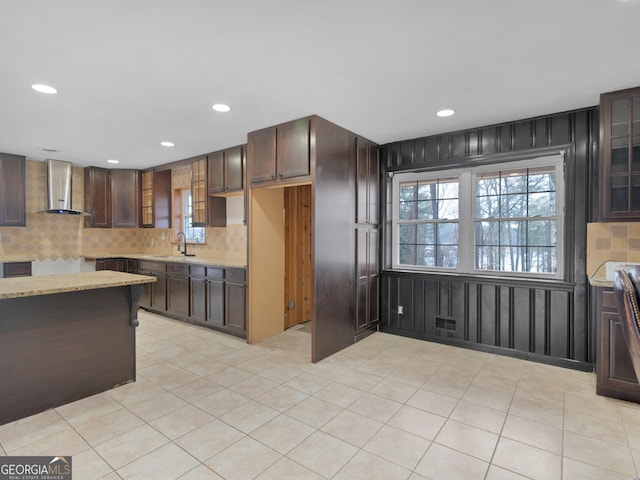 kitchen featuring dark brown cabinetry, light stone countertops, sink, wall chimney exhaust hood, and wood walls