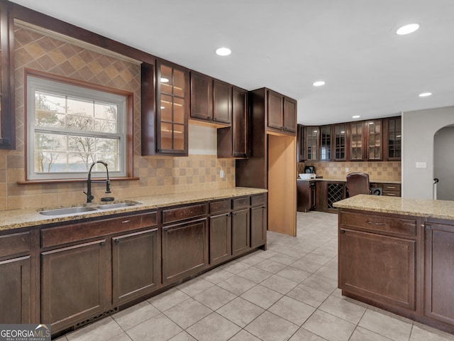 kitchen with dark brown cabinetry, light stone counters, and sink