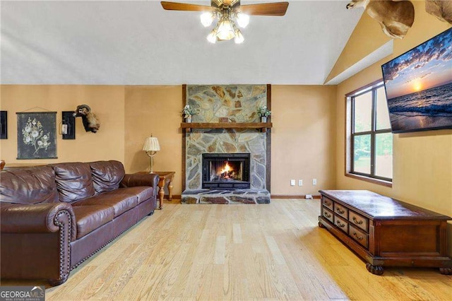 living room featuring ceiling fan, a stone fireplace, light wood-type flooring, and vaulted ceiling