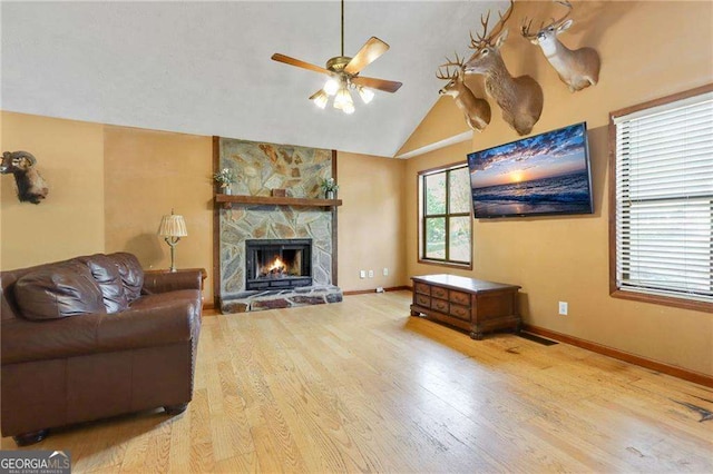 living room featuring light hardwood / wood-style flooring, vaulted ceiling, ceiling fan, and a stone fireplace