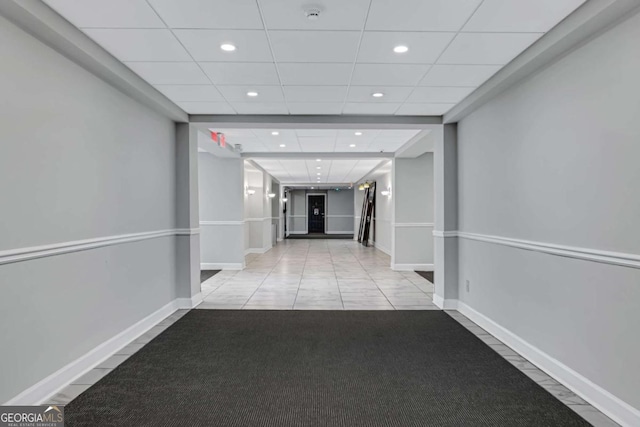 corridor with light tile patterned floors and a paneled ceiling