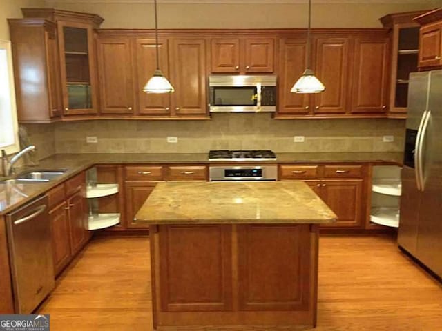 kitchen with light wood-type flooring, stainless steel appliances, sink, pendant lighting, and a kitchen island