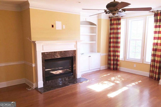 unfurnished living room featuring a high end fireplace, hardwood / wood-style flooring, ceiling fan, and ornamental molding