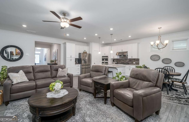 living room with ceiling fan with notable chandelier, light hardwood / wood-style floors, and ornamental molding