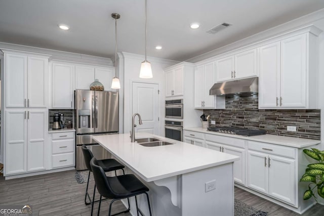 kitchen featuring white cabinetry, sink, stainless steel appliances, pendant lighting, and a kitchen island with sink