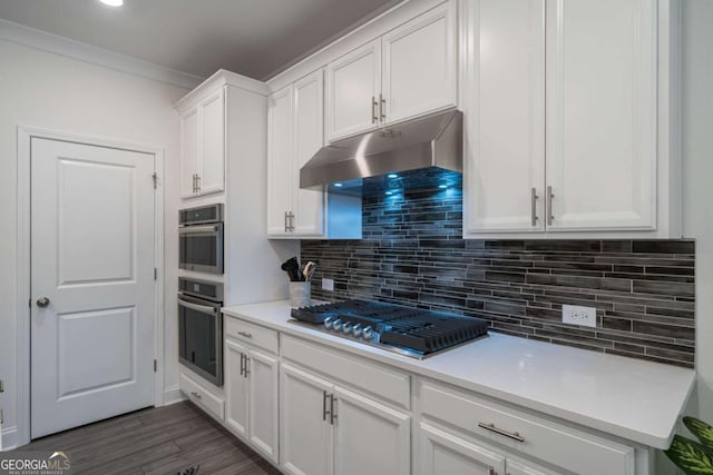 kitchen with crown molding, dark hardwood / wood-style floors, appliances with stainless steel finishes, tasteful backsplash, and white cabinetry