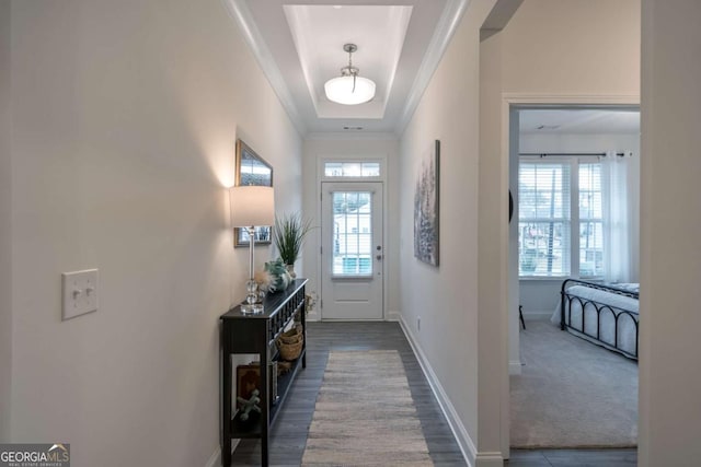 doorway featuring a tray ceiling, dark carpet, and crown molding