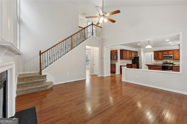 unfurnished living room featuring ceiling fan, a towering ceiling, and dark wood-type flooring