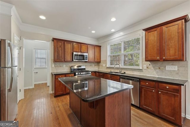 kitchen with sink, light wood-type flooring, ornamental molding, a kitchen island, and stainless steel appliances