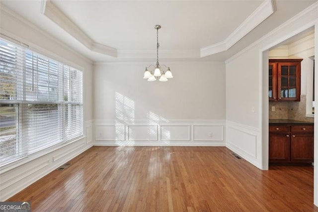 unfurnished dining area with a healthy amount of sunlight, wood-type flooring, crown molding, and a tray ceiling