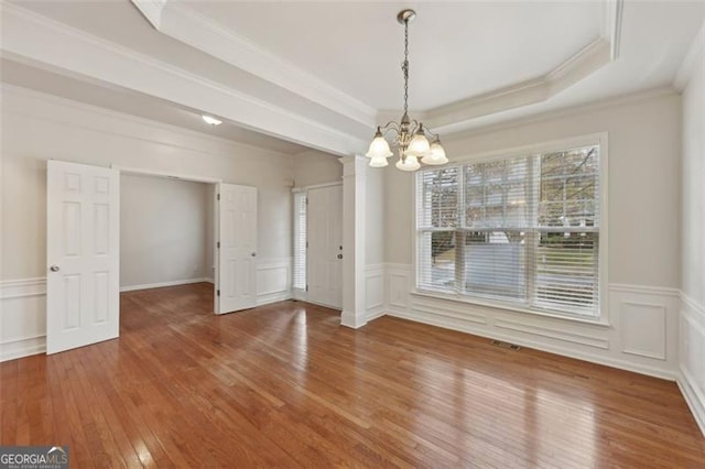 unfurnished dining area with a raised ceiling, hardwood / wood-style floors, a chandelier, and ornamental molding