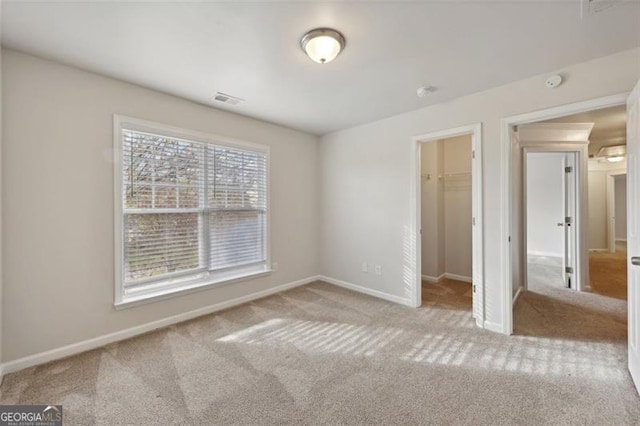 unfurnished bedroom featuring a spacious closet, a closet, and light carpet