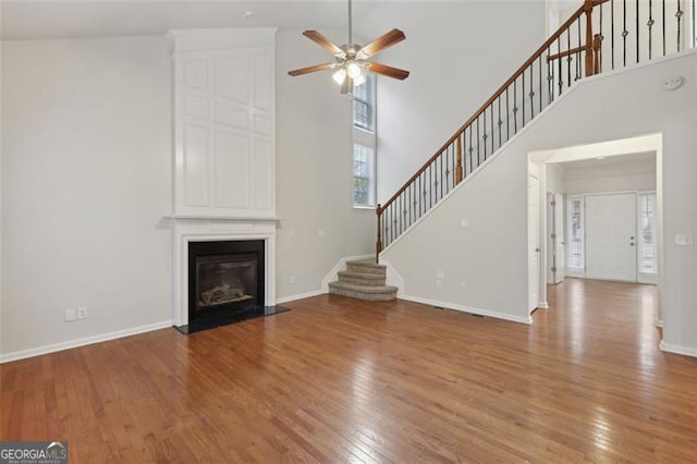 unfurnished living room with ceiling fan, a large fireplace, light hardwood / wood-style floors, and a high ceiling