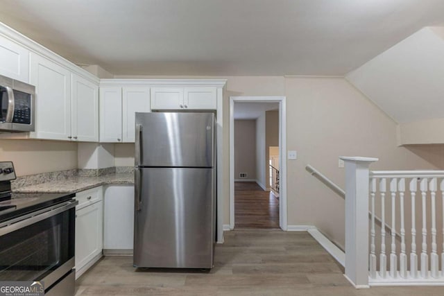 kitchen with white cabinets, vaulted ceiling, light stone countertops, light wood-type flooring, and appliances with stainless steel finishes