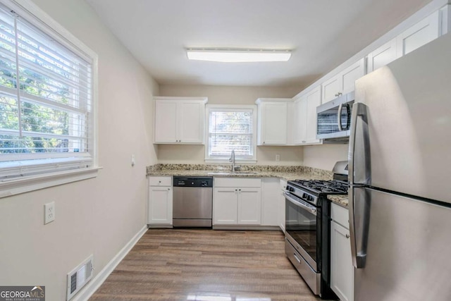 kitchen featuring light stone countertops, appliances with stainless steel finishes, light wood-type flooring, sink, and white cabinets