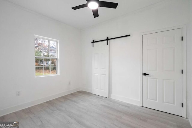 unfurnished bedroom featuring ceiling fan, a barn door, light wood-type flooring, and crown molding