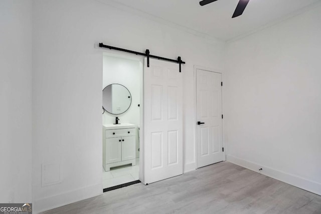 unfurnished bedroom featuring sink, ceiling fan, a barn door, connected bathroom, and light hardwood / wood-style floors