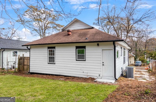 rear view of property with central air condition unit and a lawn