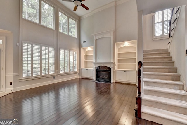 unfurnished living room featuring a wealth of natural light, dark hardwood / wood-style flooring, a towering ceiling, and ceiling fan