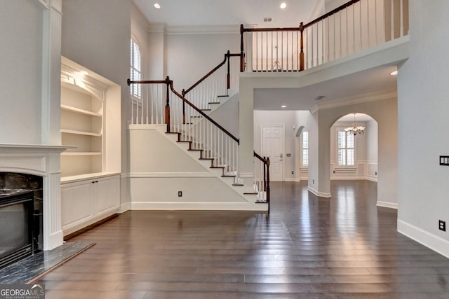 unfurnished living room featuring ornamental molding, dark wood-type flooring, a high end fireplace, and a high ceiling