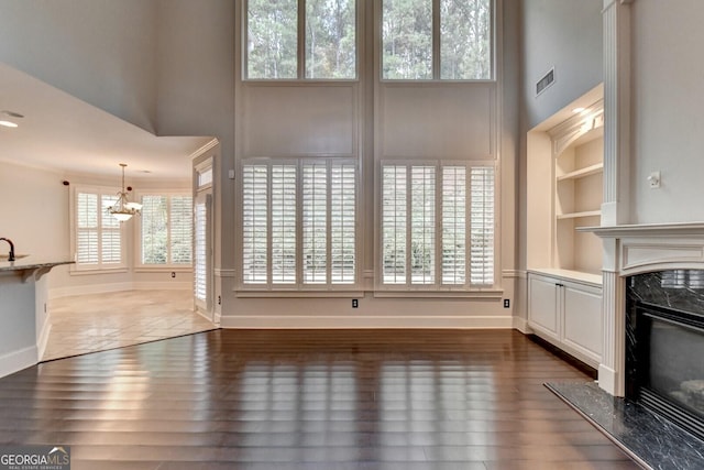 unfurnished living room featuring a fireplace, a chandelier, built in features, and dark wood-type flooring