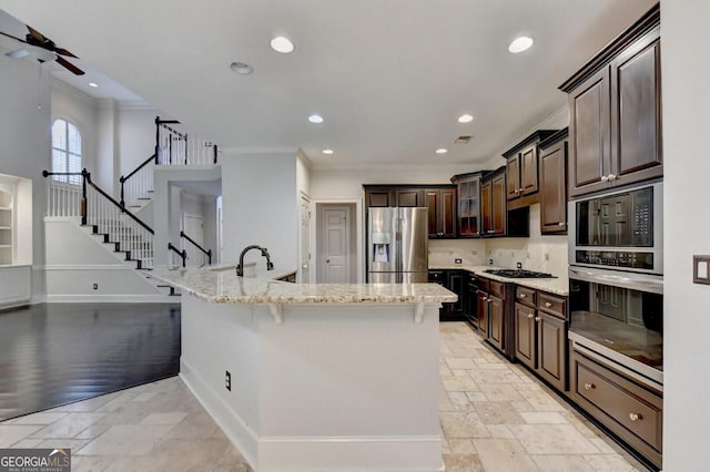 kitchen featuring light stone counters, a breakfast bar, appliances with stainless steel finishes, dark brown cabinets, and ornamental molding