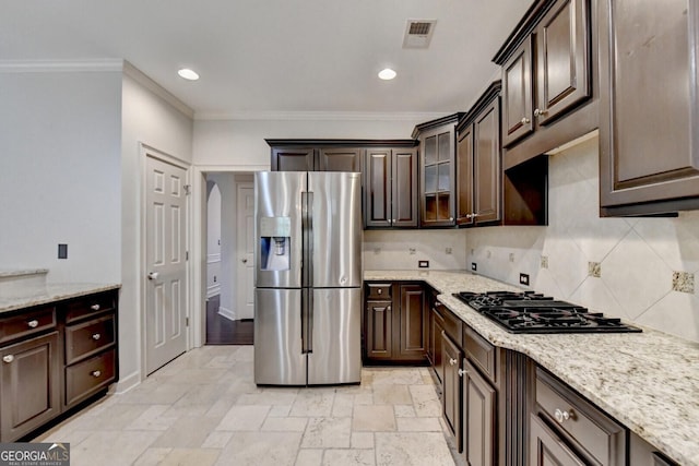 kitchen with dark brown cabinetry, light stone countertops, stainless steel appliances, tasteful backsplash, and ornamental molding